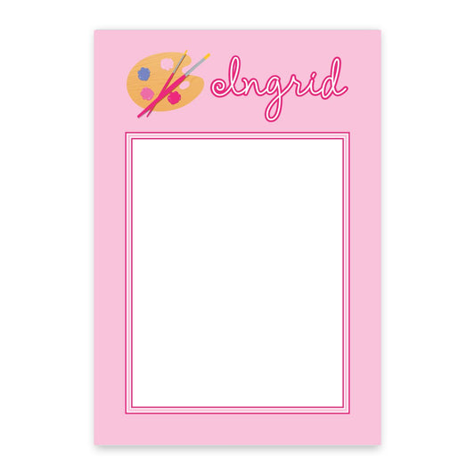 The Noteworthy Pink Artist Personalized Notepad features a pink border, blank white center, painter’s palette with brushes at the top, and is customized with the name "Ingrid" in cursive.