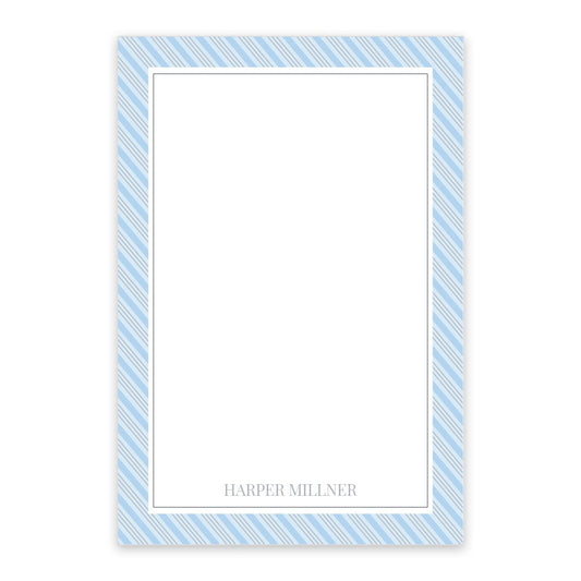 The Blue Pinstripe Personalized Notepad by Noteworthy features a vertical design with a blue and white diagonal border and your name in gray at the bottom. Available in 50 or 100 sheets for personalized notes.