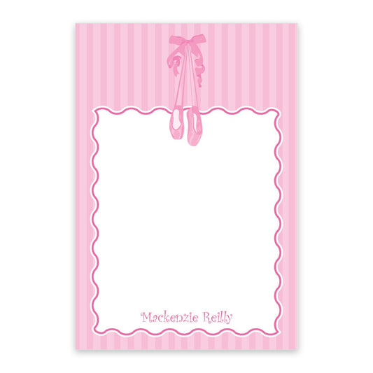 The Ballet Slippers Personalized Notepad by Noteworthy features pink stripes, ballet slippers at the top, a wavy border framing a blank space, and “Mackenzie Reilly” printed at the bottom.
