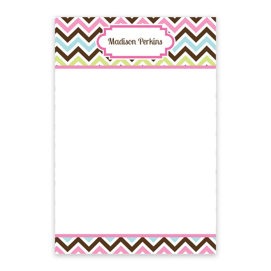 The Noteworthy Multi-Color Chevron Personalized Notepad features a vibrant chevron border in pink, brown, blue, and green with "Madison Perkins" at the top center and a blank white space for writing.