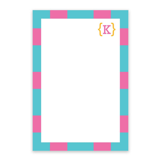 The Noteworthy Preppy Stripes Personalized Notepad features a teal rectangular design with a blue and pink checkerboard border, a yellow bracketed "K" at the top right, a blank center for notes, and includes 100 sheets.