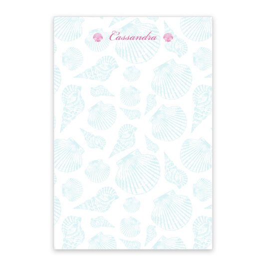 The Noteworthy Blue Shell Pattern Personalized Notepad features blue sea shells and two pink shells at the top, with “Cassandra” in pink cursive. Contains 100 sheets.