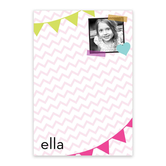 The Noteworthy Chevron Flags Personalized Notepad with Photo features a pink chevron pattern, colorful banner accents, your child's black-and-white photo, and their name printed at the bottom left.