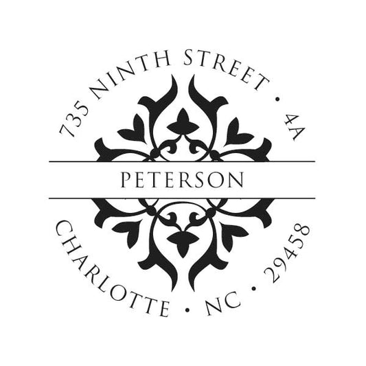 The Noteworthy Ornate Diamond Band Stamper features a circular black and white design personalized with "Peterson" and "735 Ninth Street, 4A, Charlotte, NC 29458"—a stylish self-inking stamp for all your mailing needs.