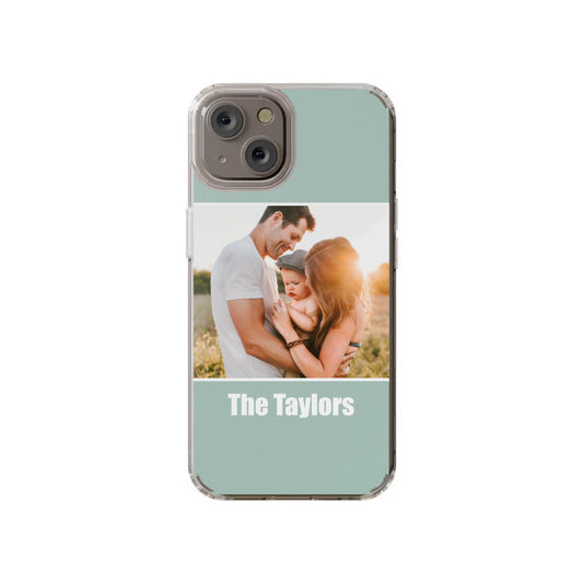 Showcase your family photo with the Custom Color Block iPhone 14 Clear Case from InvitationBox.com, featuring a picture of two adults and a baby outdoors and "The Taylors" printed beneath the image.